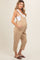 woman wearing a beige maternity overall with buttons and pockets, showing her baby bump