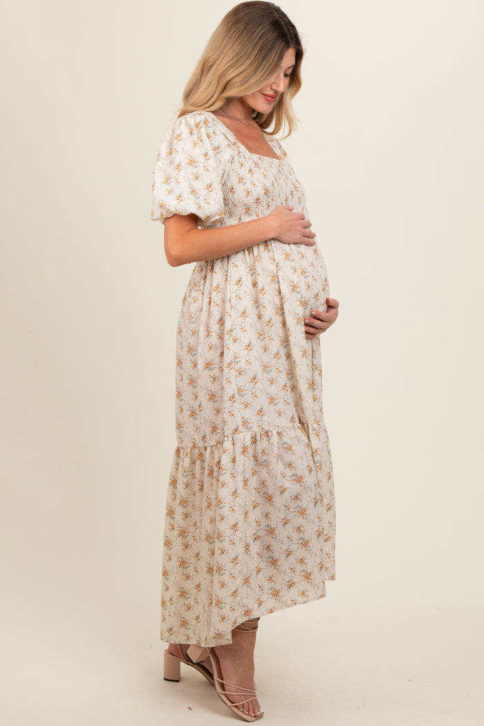 woman wearing a cream floral maternity maxi dress with puff sleeves and a tiered skirt, highlighting her baby bump