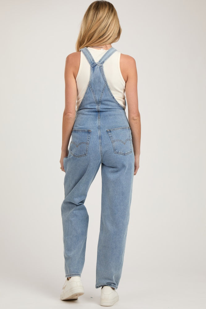 woman wearing light blue maternity overalls with a fitted white tank top underneath, showing a relaxed fit and adjustable straps