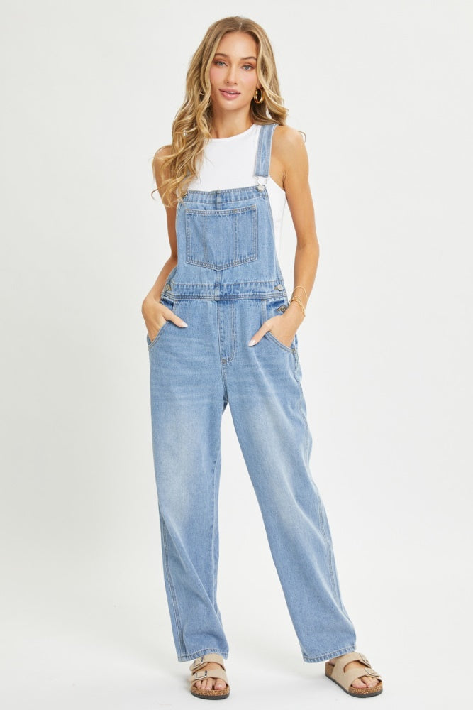 woman wearing light blue denim overalls with pockets, paired with a white tank top and sandals