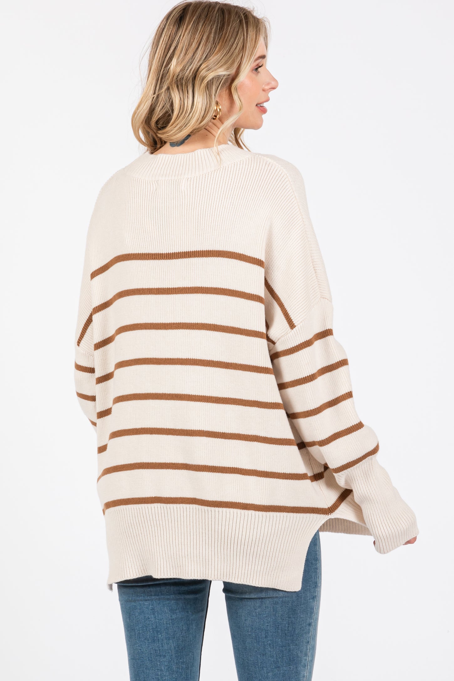 woman wearing a cream and brown striped oversized sweater with a rounded hem and long sleeves