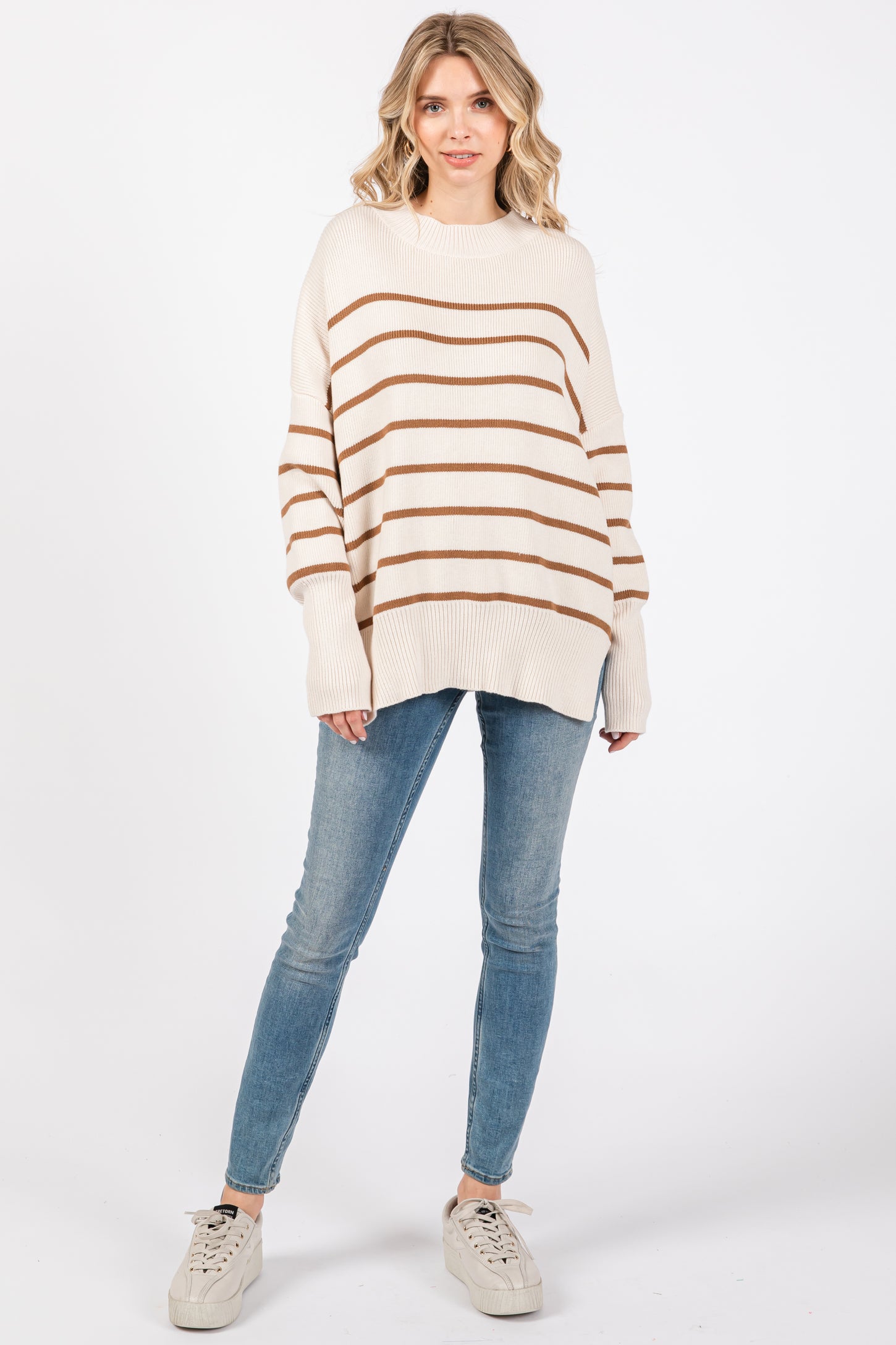 woman wearing a cream and brown striped oversized sweater with blue skinny jeans and white sneakers