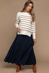 woman wearing a cream and brown striped maternity sweater and a navy tiered maxi skirt, holding her baby bump