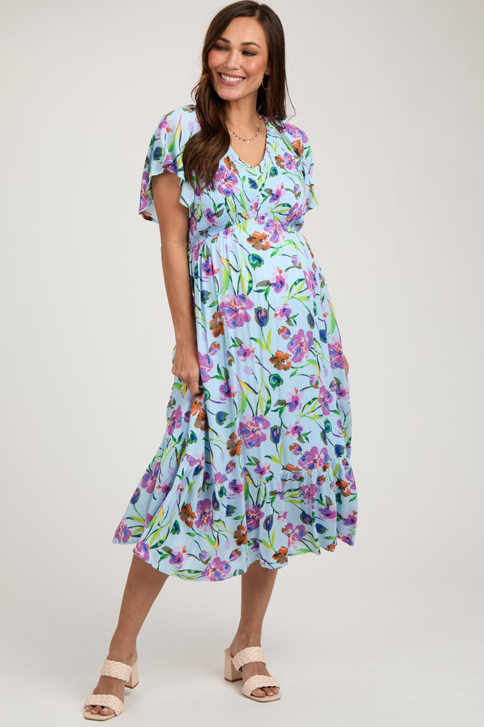 woman wearing a light blue floral maternity dress with short flutter sleeves and a flowy skirt, showing her baby bump