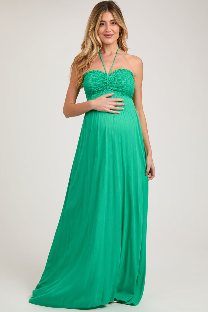 woman wearing a green halter neck maternity maxi dress and holding her baby bump