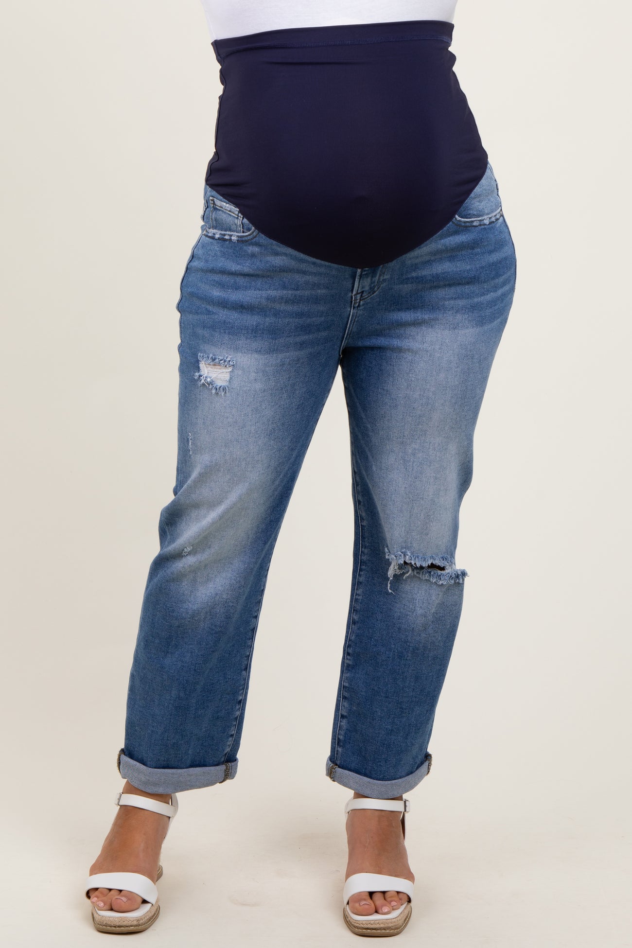 woman wearing dark blue maternity plus jeans with a high waist, featuring distressed details and rolled cuffs, showing a baby bump