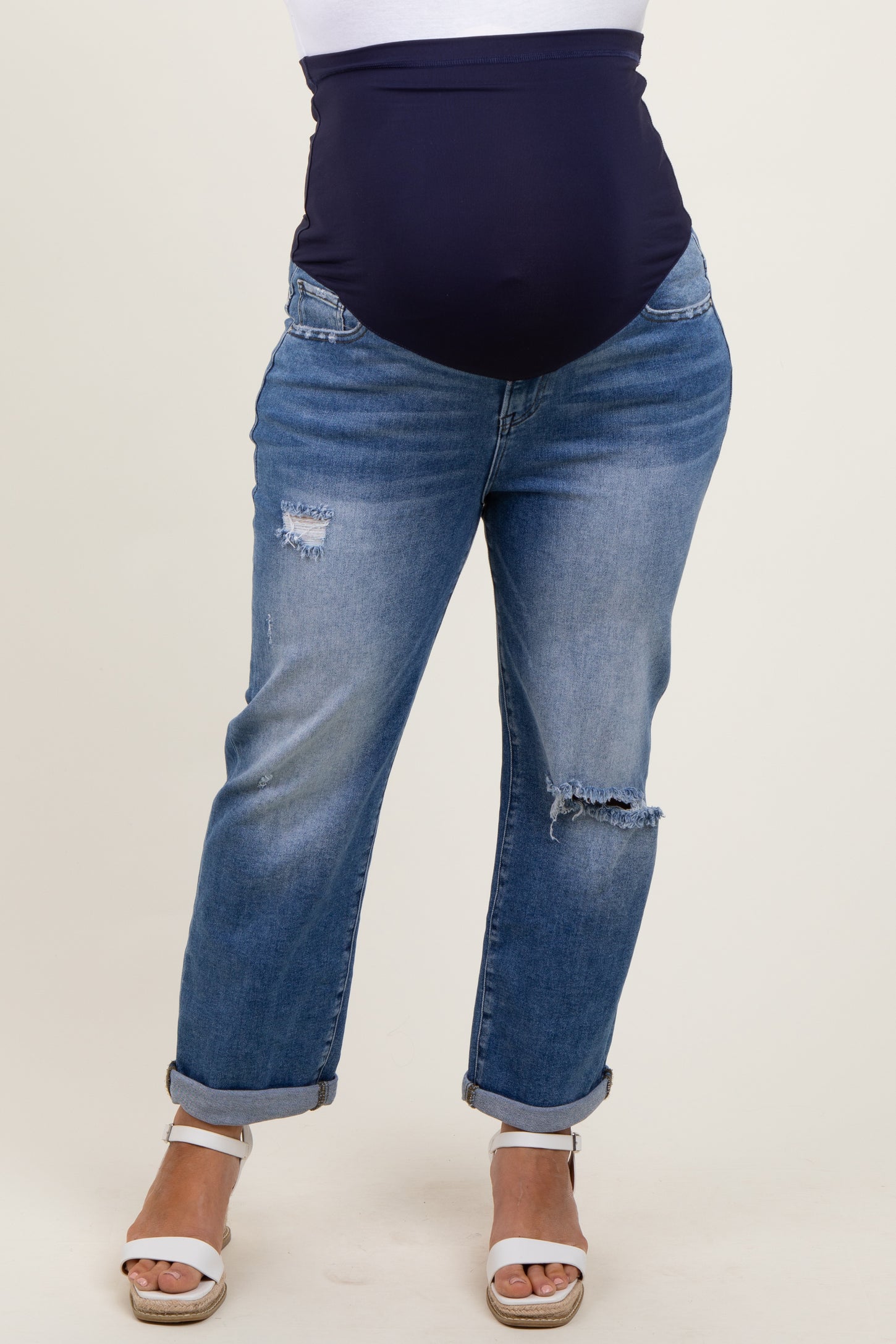 woman wearing dark blue maternity plus jeans with a high waist, featuring distressed details and rolled cuffs, showing a baby bump