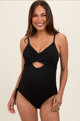 woman wearing a black maternity swimsuit with a twisted front and cut-out detail, showing her baby bump
