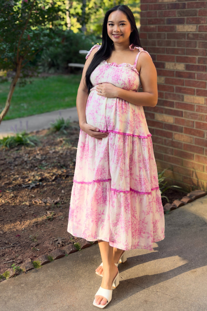 woman wearing a pink floral maternity dress with ruffle straps and holding her baby bump