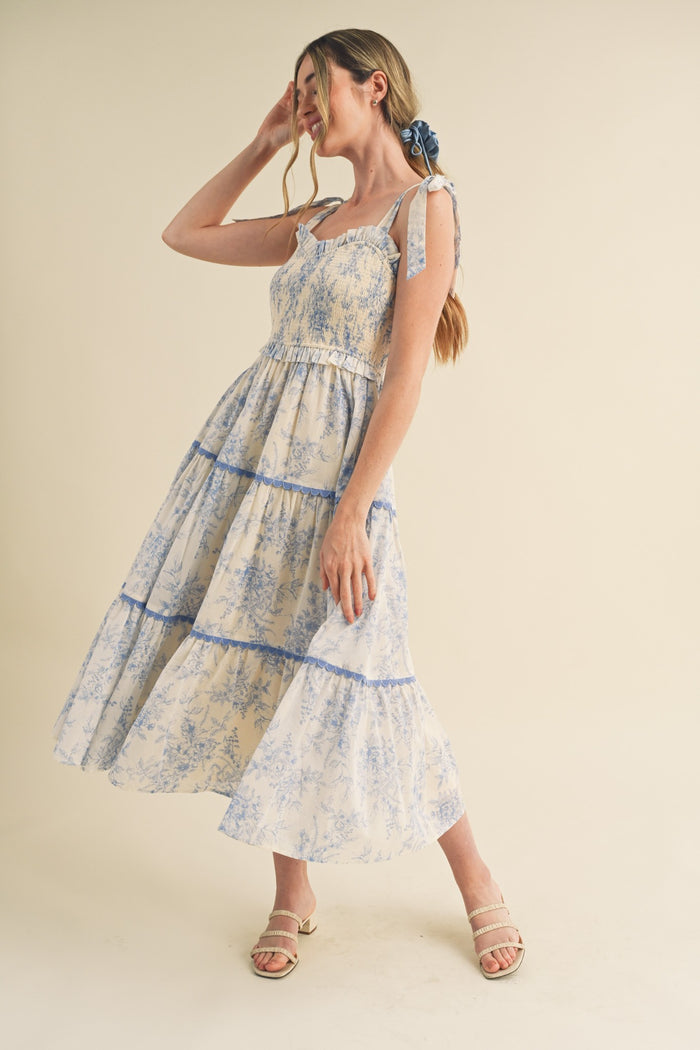 woman wearing a floral print maxi dress with blue and white tones, tied straps, and a flowing skirt