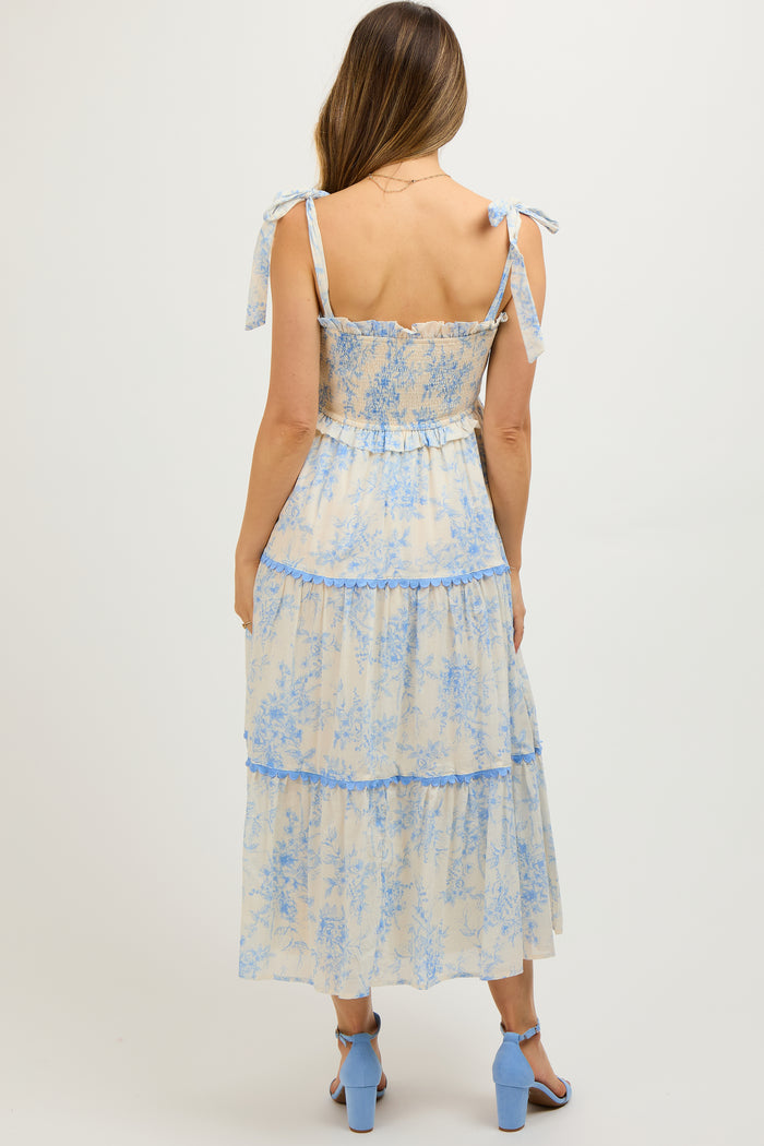 woman wearing a blue and cream floral print maternity dress with tie straps and tiered skirt, showing a baby bump