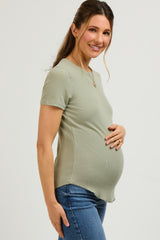 woman wearing a light green ribbed maternity top and holding her baby bump while smiling
