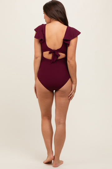 woman wearing a maroon maternity one-piece swimsuit with ruffle details and a tied back, showcasing a baby bump