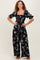 woman wearing a black floral print jumpsuit with puff sleeves and a square neckline