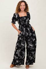 woman wearing a black floral print jumpsuit with puff sleeves and pockets, smiling at the camera
