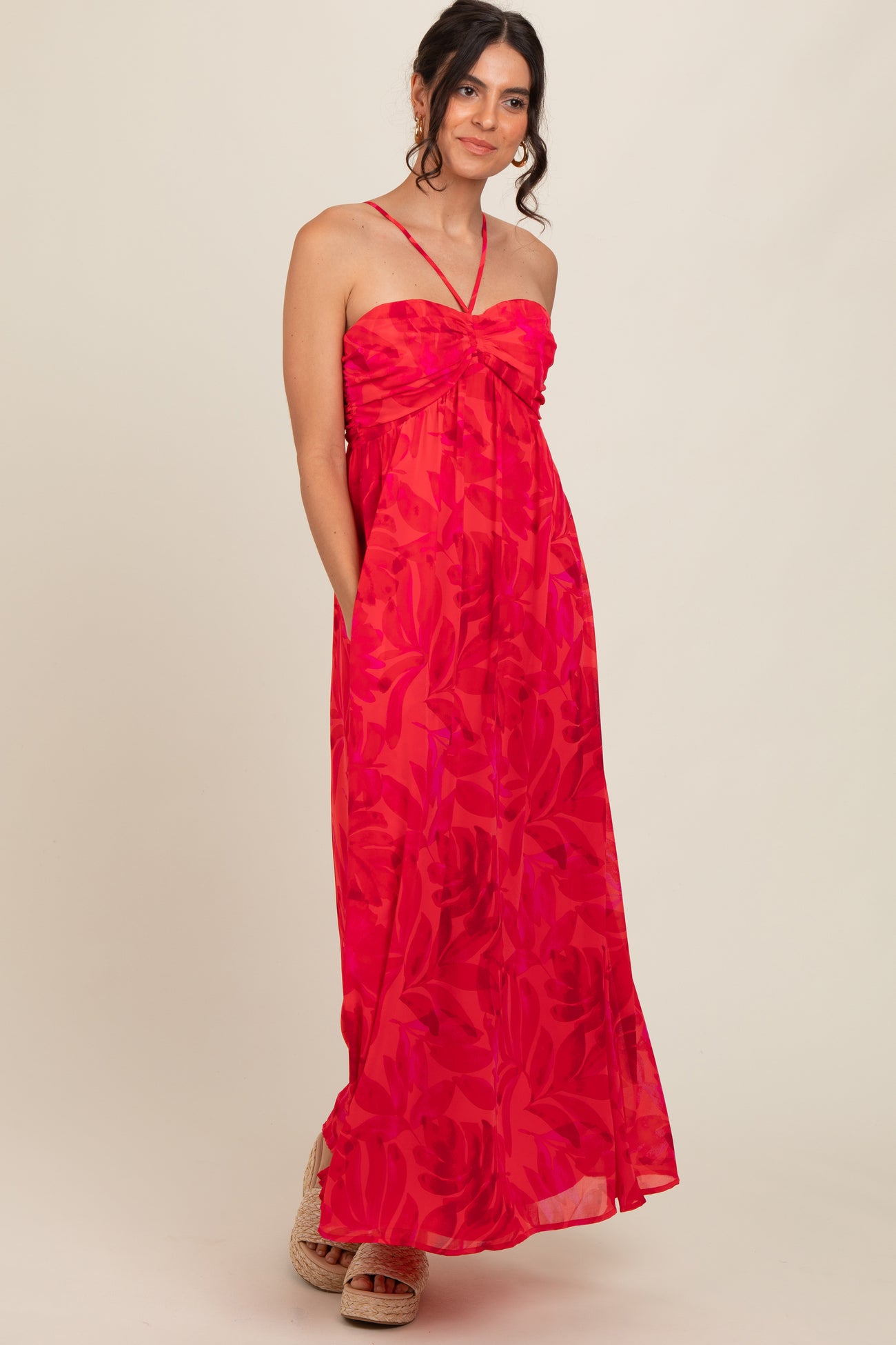 woman wearing a bright pink floral maxi dress with a tie detail at the neckline and side pockets