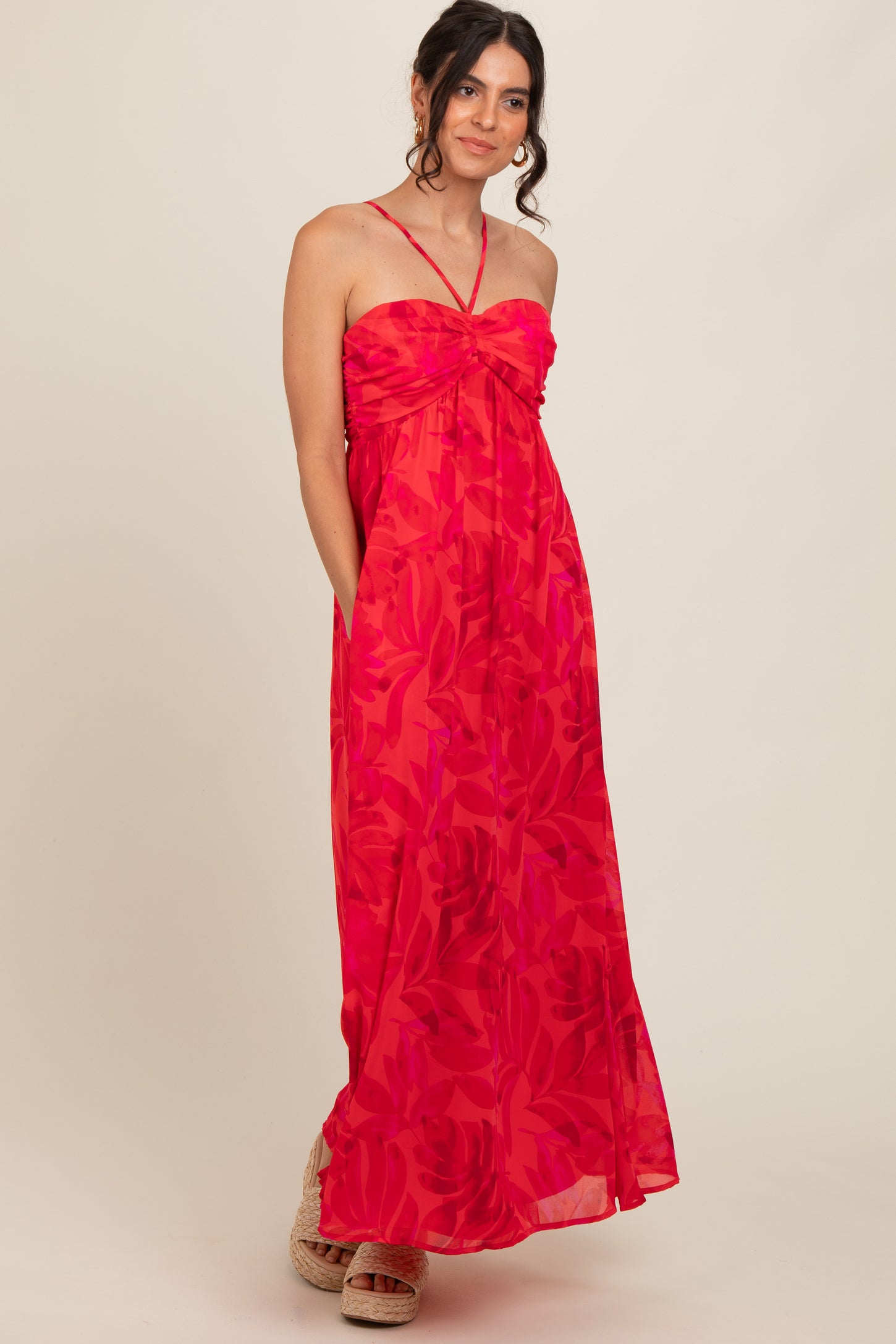 woman wearing a bright pink floral maxi dress with a tie detail at the neckline and side pockets