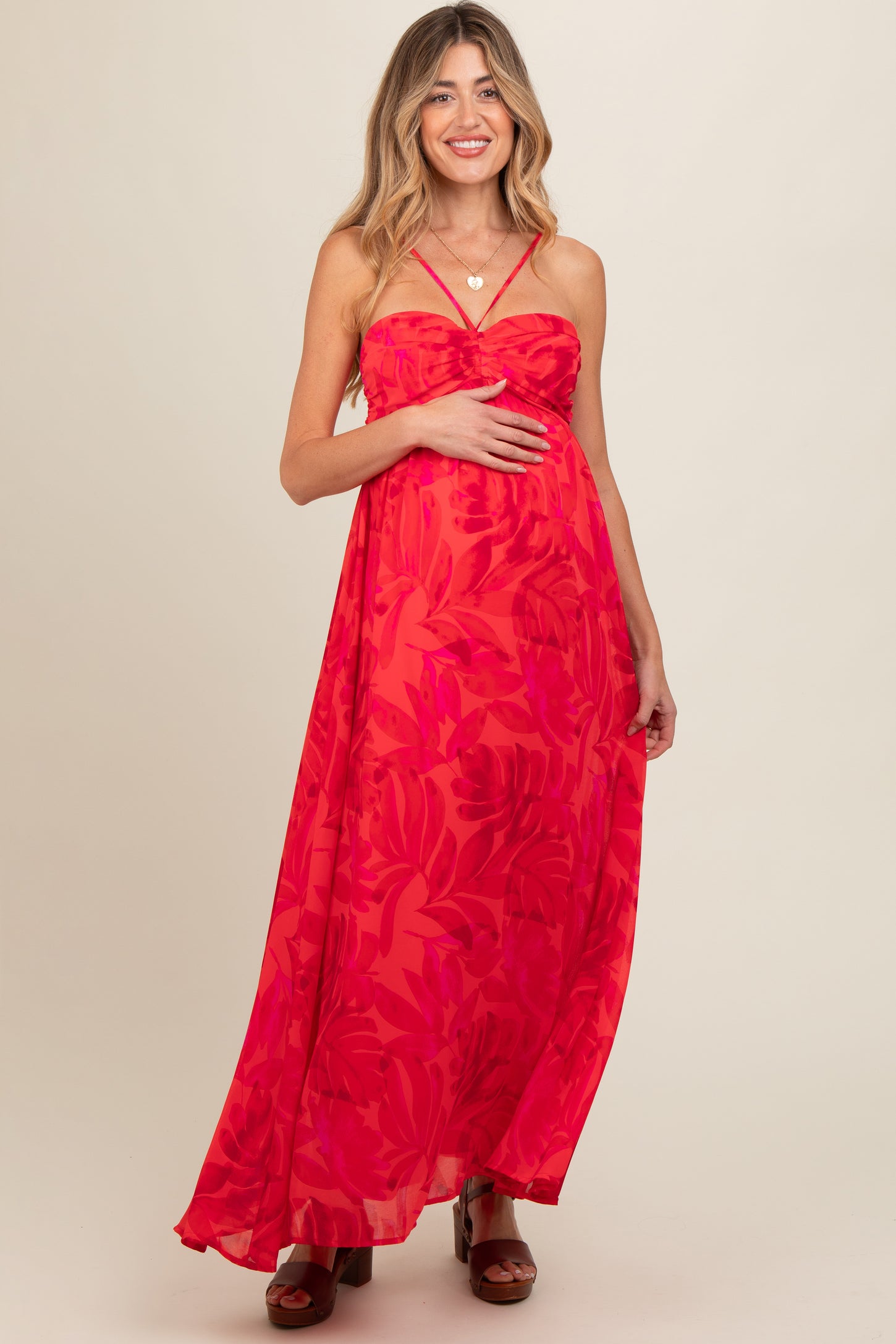 woman wearing a bright floral print maternity maxi dress and holding her baby bump
