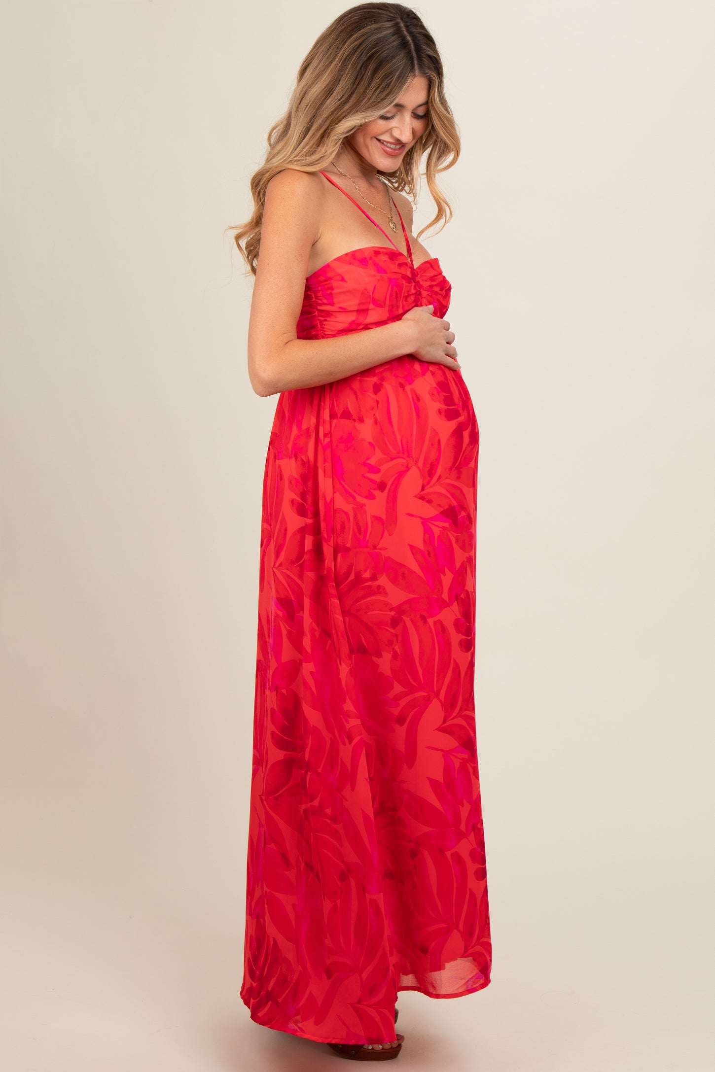 woman wearing a red floral maternity maxi dress and holding her baby bump