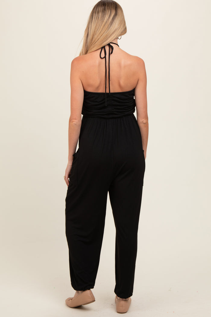 woman wearing a black maternity jumpsuit with a halter neck and gathered back details, showing a sleek silhouette
