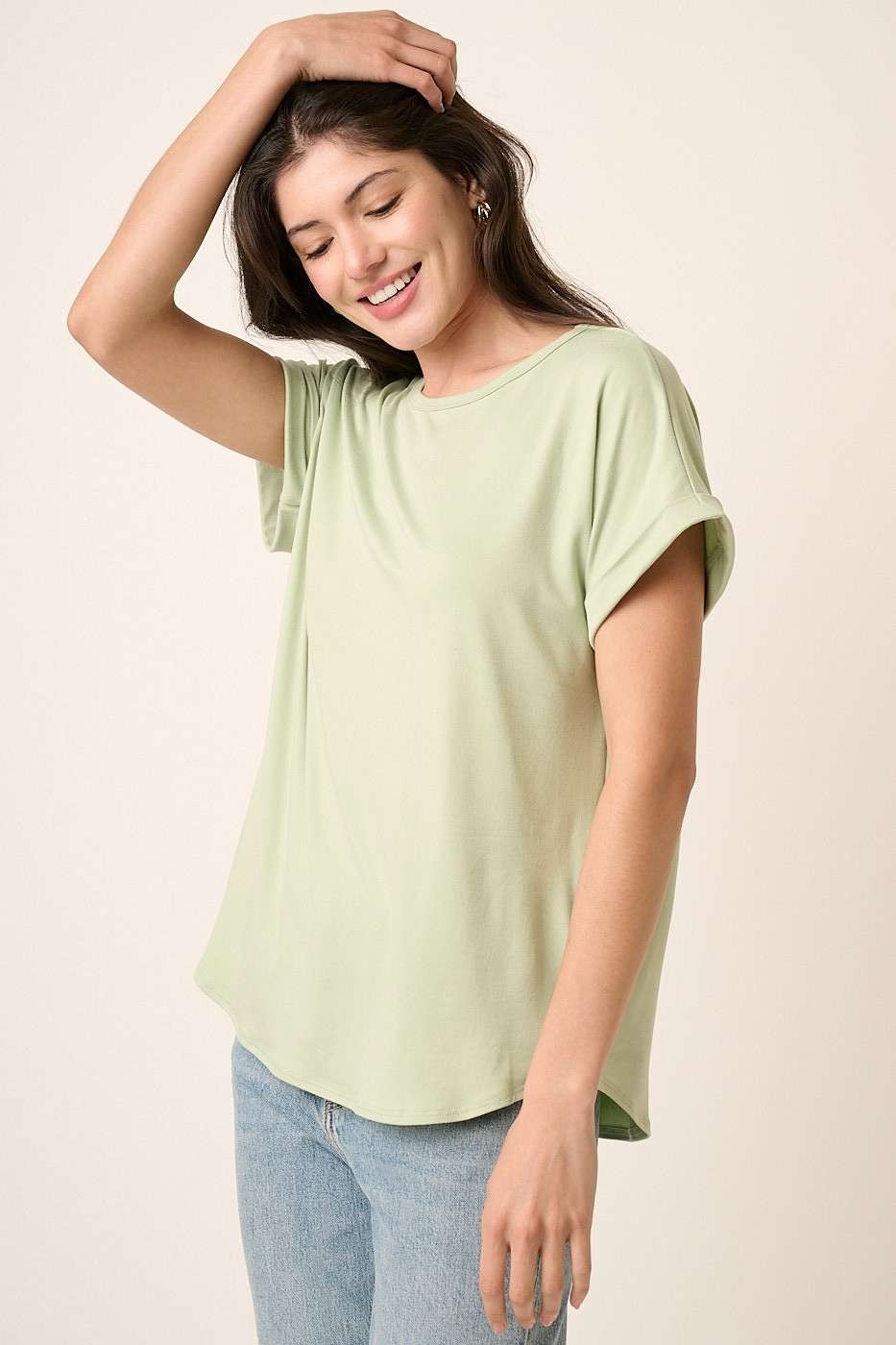 woman wearing a light green short sleeve top with rolled sleeves and a relaxed fit, smiling with one hand in her hair