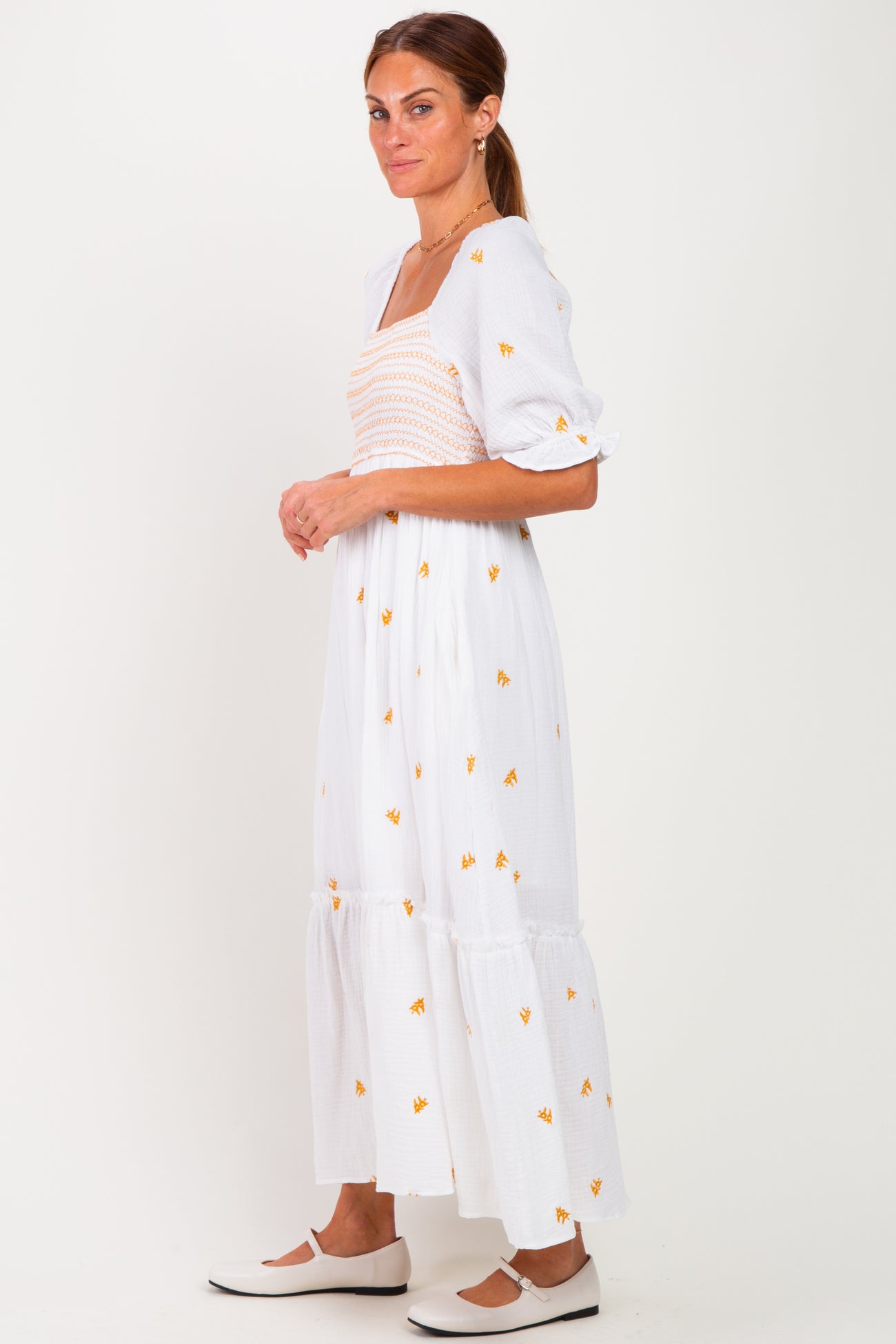 woman wearing a white floral maxi dress with puff sleeves and a smocked bodice, standing sideways against a plain background
