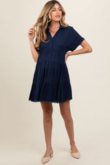 woman wearing a navy blue short sleeve maternity dress with a tiered skirt and collar, showing her baby bump