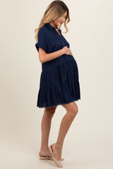 woman wearing a navy blue short sleeve maternity dress with tiered ruffle detailing and holding her baby bump