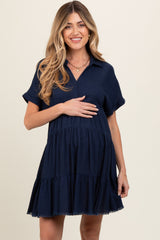 woman wearing a navy blue short sleeve maternity dress with a tiered skirt and a collar, holding her baby bump