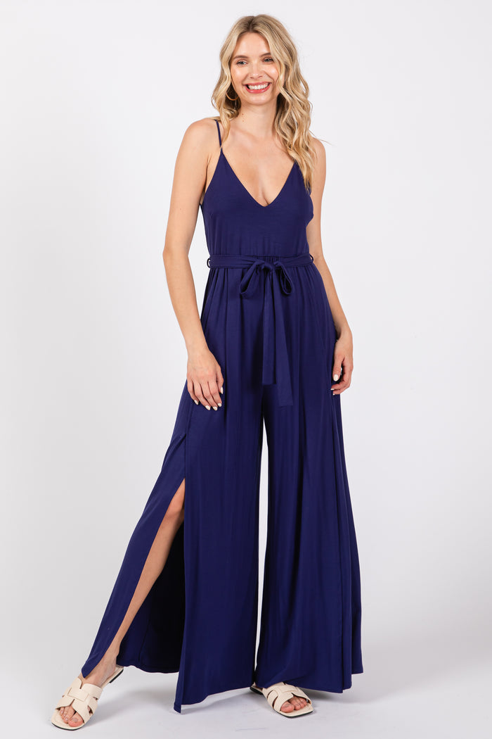 woman wearing a navy blue sleeveless jumpsuit with a tie waist and side slits