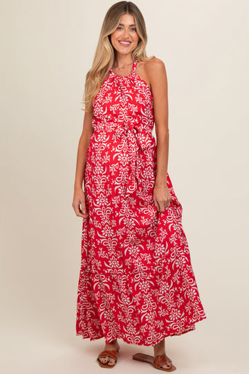 woman wearing a red floral print maternity maxi dress with a halter neckline and tie waist, showing a baby bump