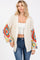 woman wearing a cream crochet cardigan with colorful patterned sleeves and a white crop top, paired with blue jeans