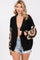 woman wearing a black chunky cardigan with crochet pattern sleeves and styled with a beige top and denim shorts