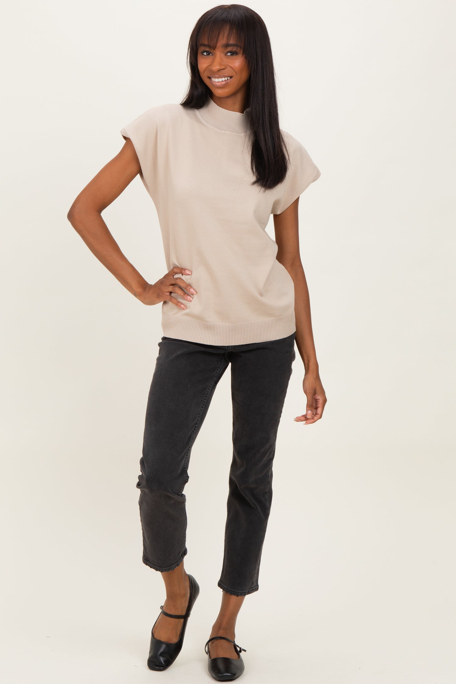 woman wearing a beige short sleeve top and black cropped jeans, standing and smiling at the camera