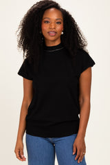woman wearing a black short sleeve sweater with a high neckline and ribbed hem, standing against a light background