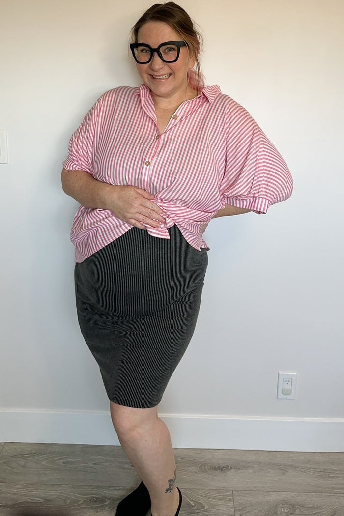 woman wearing a pink and white striped maternity shirt knotted at the waist and a black striped maternity skirt, showing baby bump
