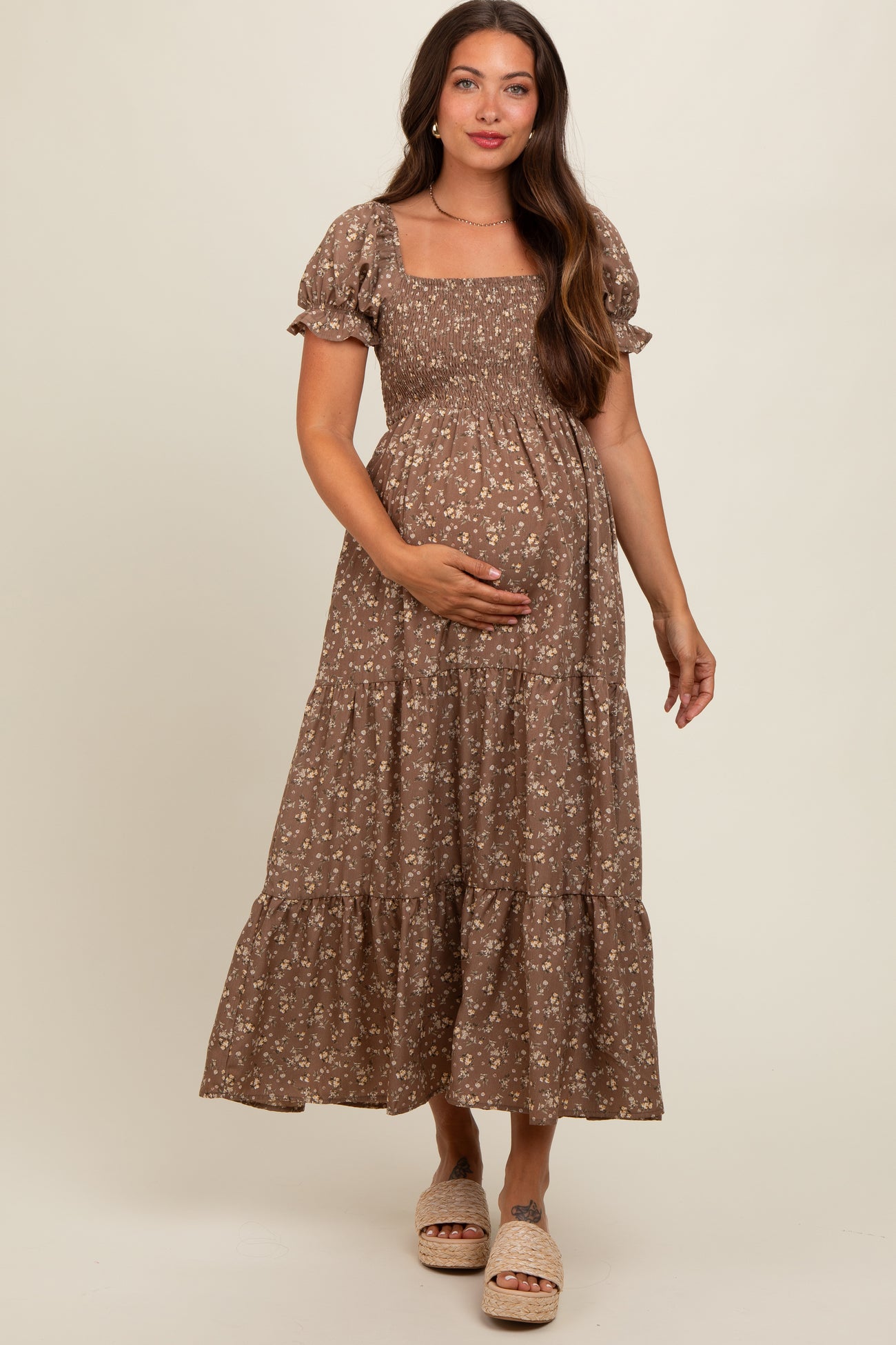 woman wearing a brown floral maternity maxi dress with puff sleeves, holding her baby bump