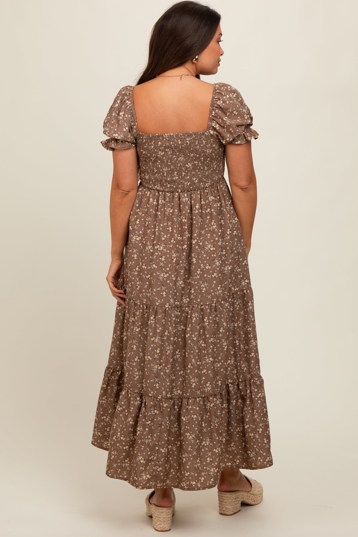 woman wearing a brown floral maternity maxi dress with puff sleeves and a smocked bodice, showcasing a baby bump