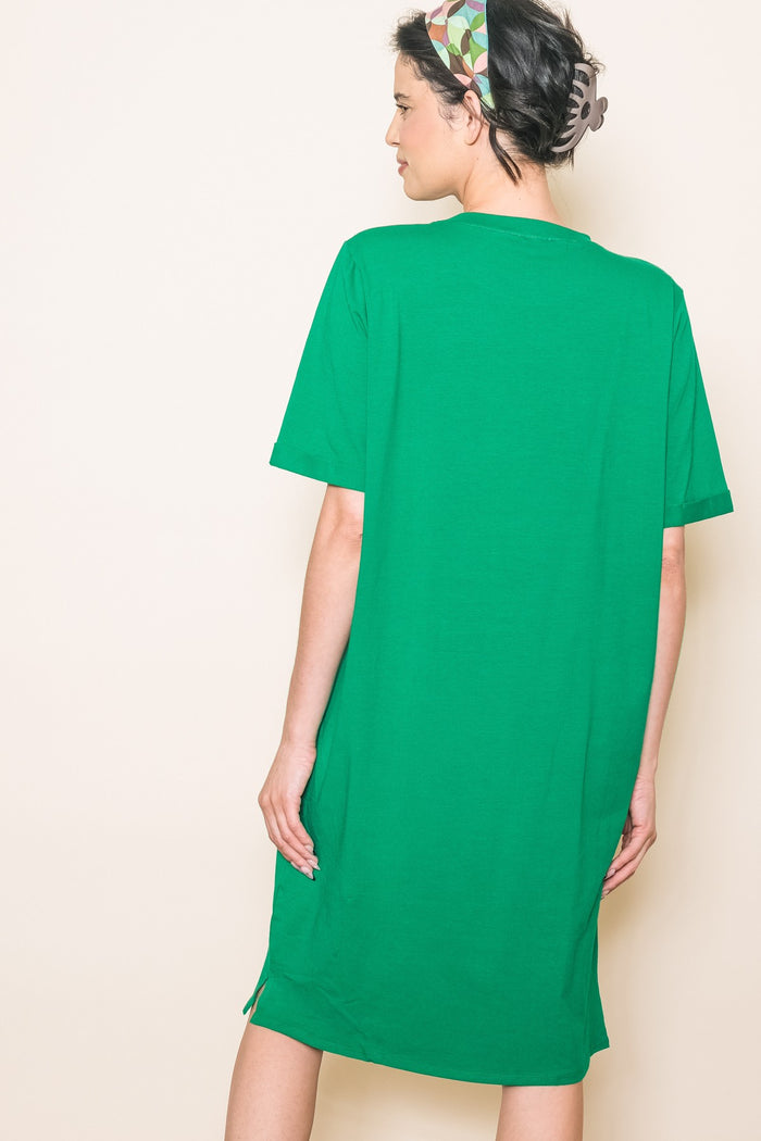 woman wearing a loose-fitting green t-shirt dress with short sleeves and side slits, viewed from the back