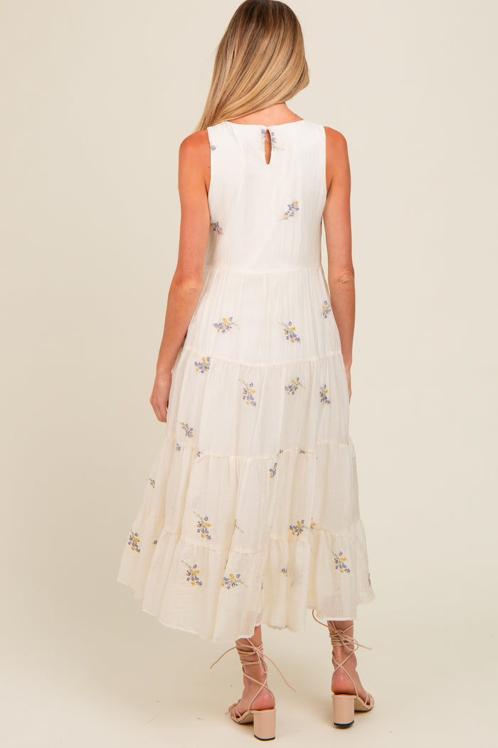 woman wearing a white tiered maternity dress with floral embroidery and a keyhole back detail