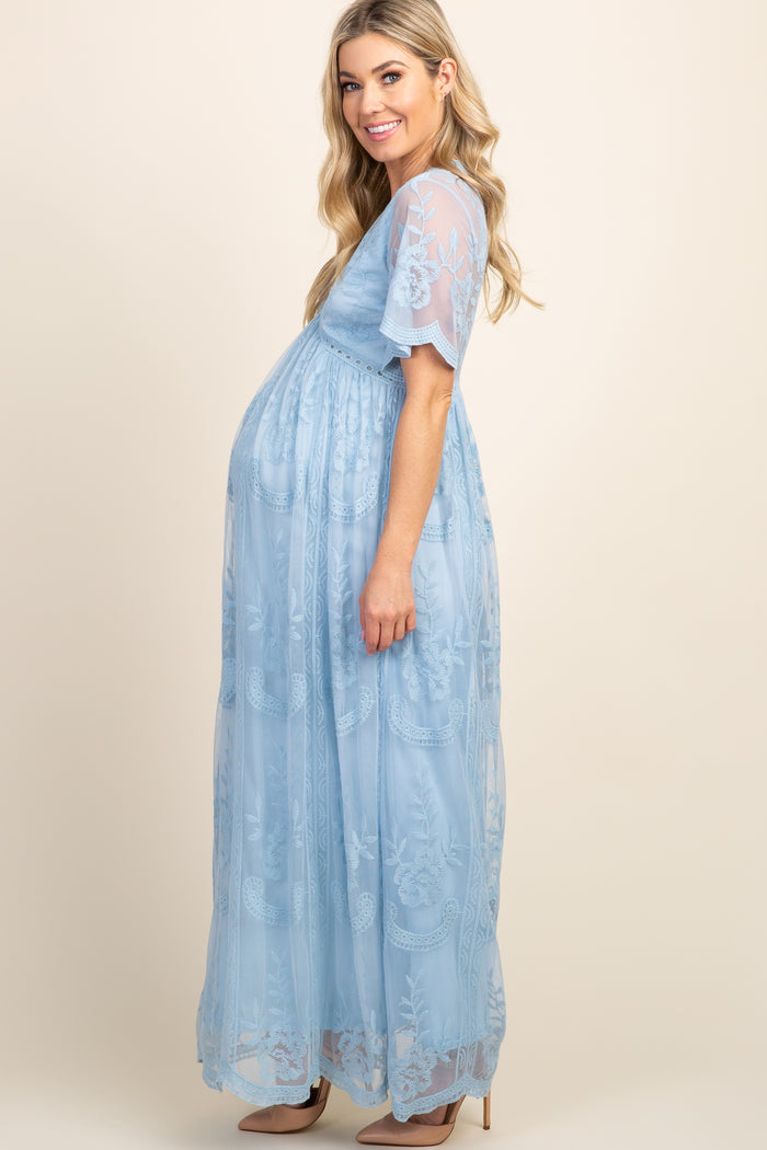 woman wearing a light blue maternity gown with floral embroidery and a visible baby bump