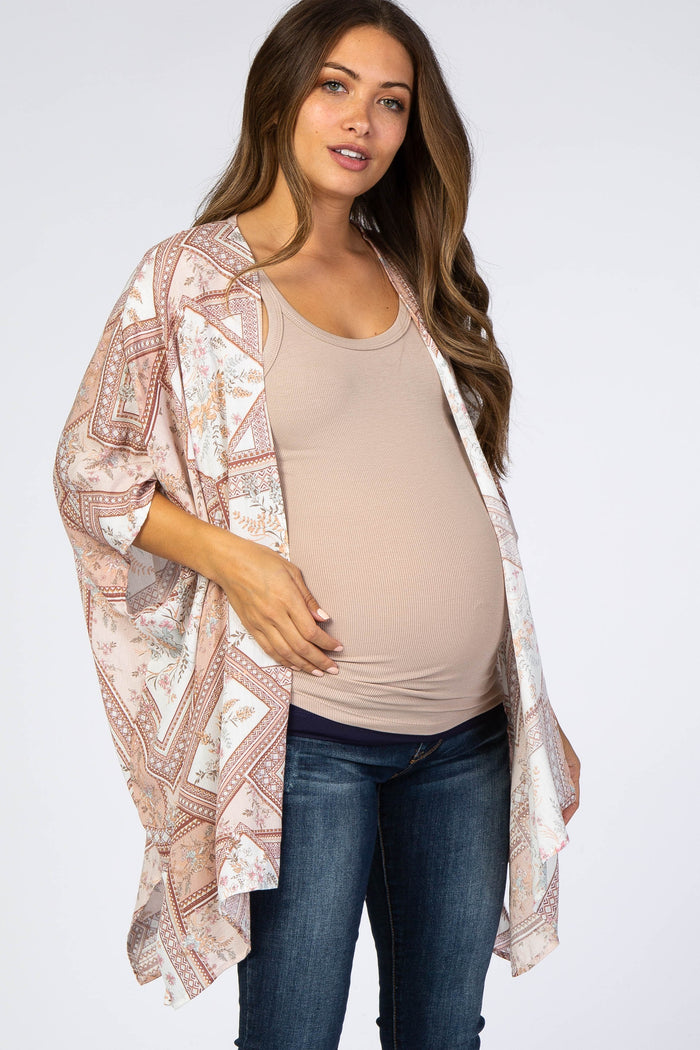 woman wearing a light pink patterned maternity kimono over a beige tank top and jeans, showcasing her baby bump