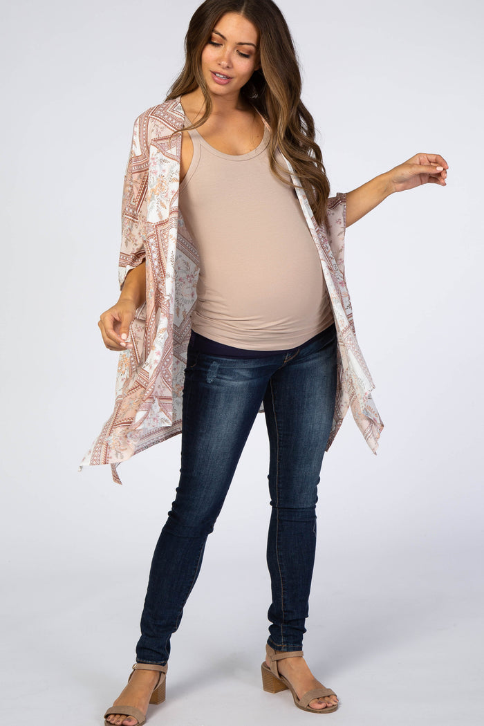 woman wearing a patterned maternity kimono over a beige tank top and blue maternity jeans, showing her baby bump