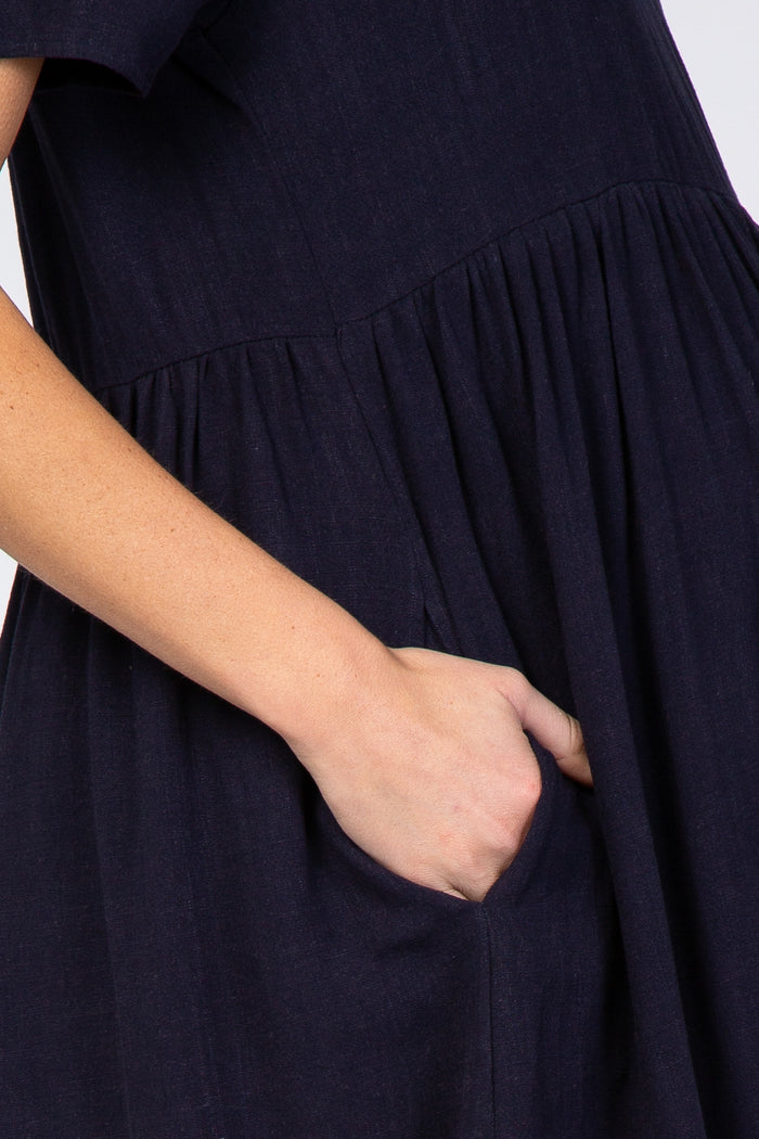 Close-up of a hand in the side pocket of a navy blue linen dress with a gathered waist
