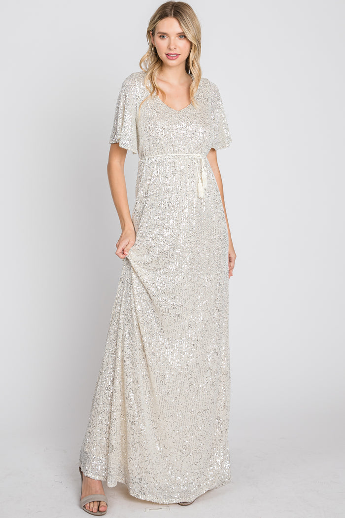 woman wearing a silver sequin maxi dress with flutter sleeves and a drawstring waist