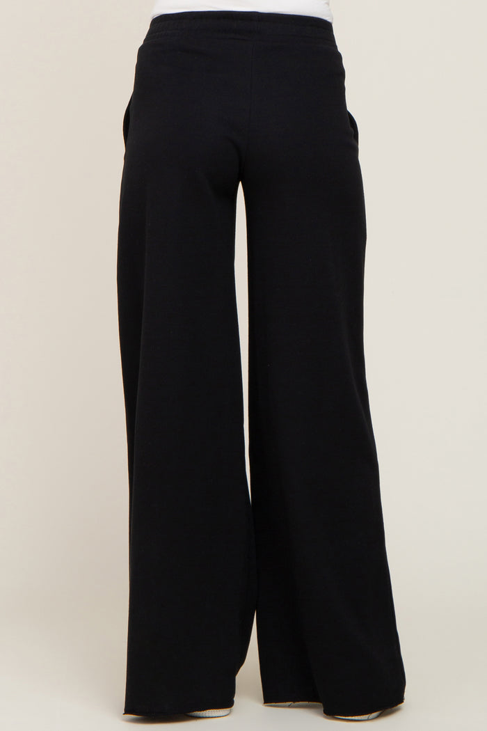 back view of person wearing black wide leg lounge pants with elastic waistband and raw hem