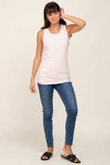 woman wearing a light pink sleeveless tank top and blue skinny jeans, standing with one hand on her hip